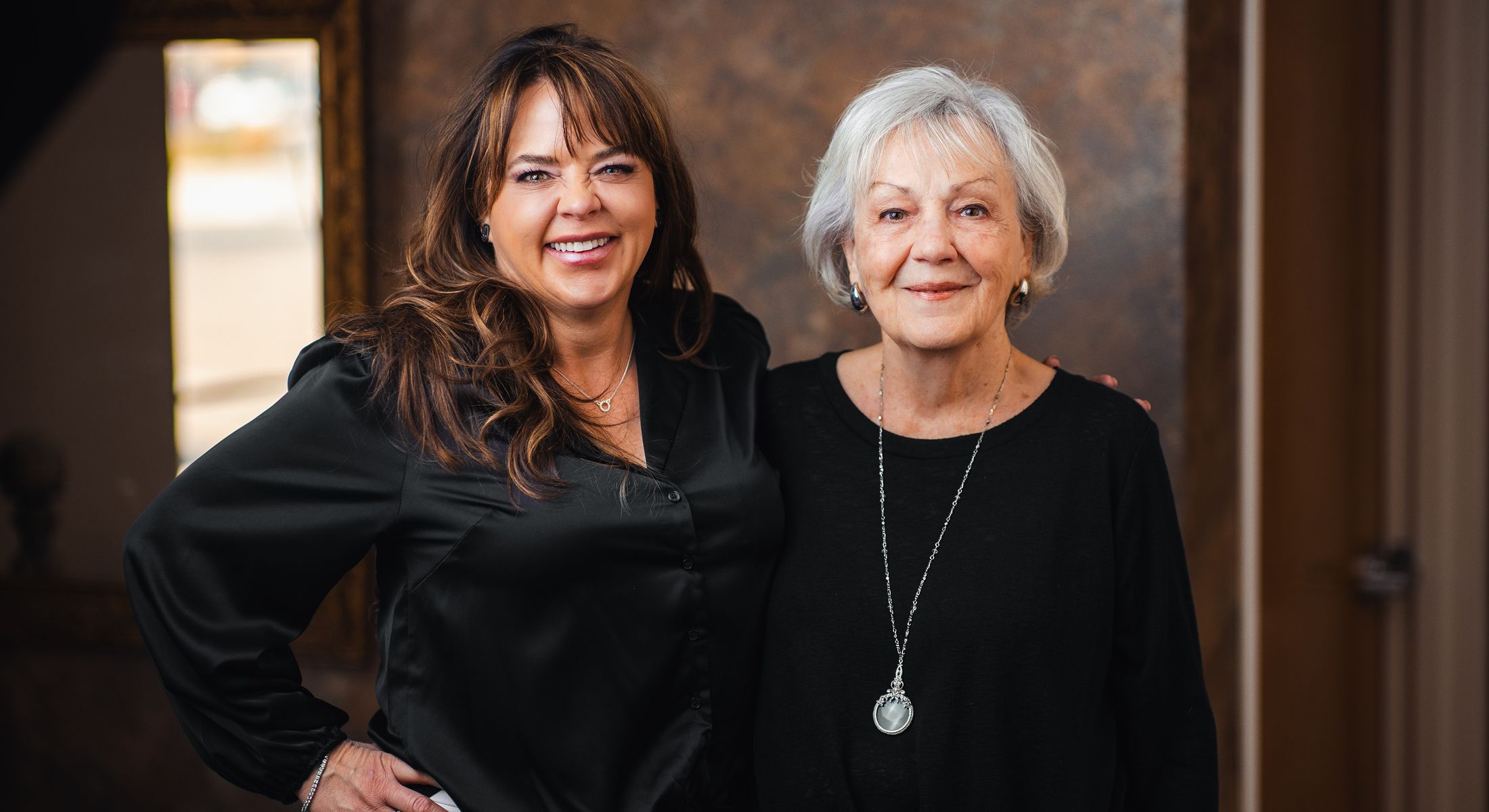 Two women smiling together in casual outfits.